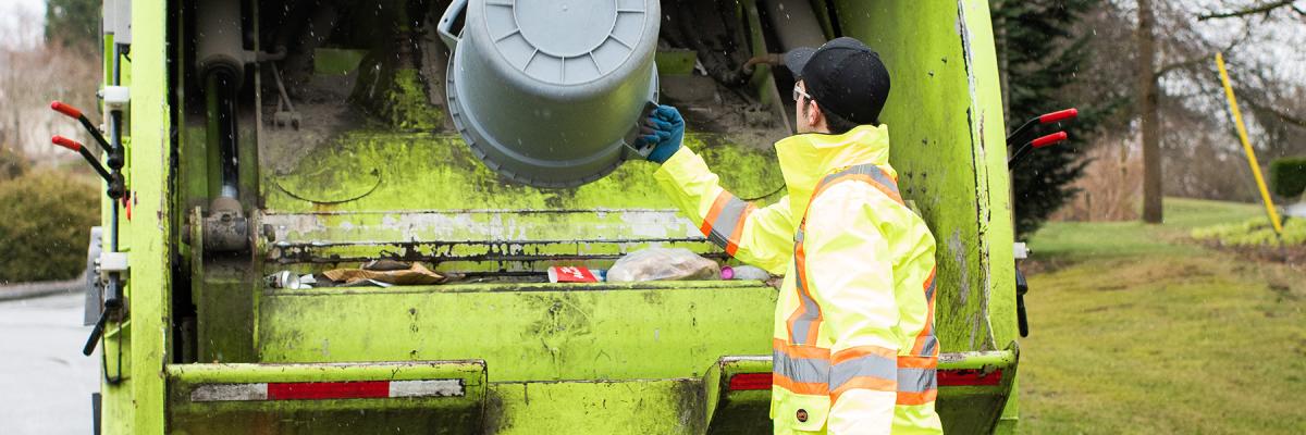 A person emptying a garbage bin into the back of a collection truck.